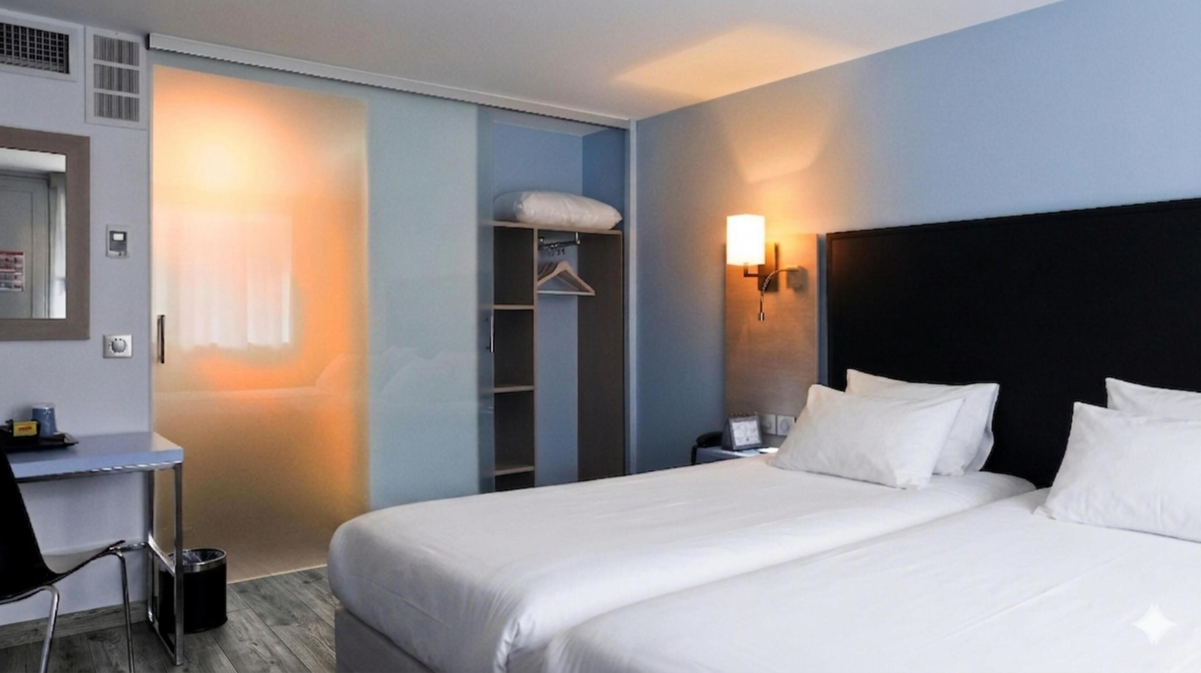 Une chambre d’hôtel comprenant un lit, une table de chevet, une lampe, une armoire et un bureau avec une chaise.