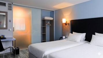 Une chambre d’hôtel comprenant un lit, une table de chevet, une lampe, une armoire et un bureau avec une chaise.