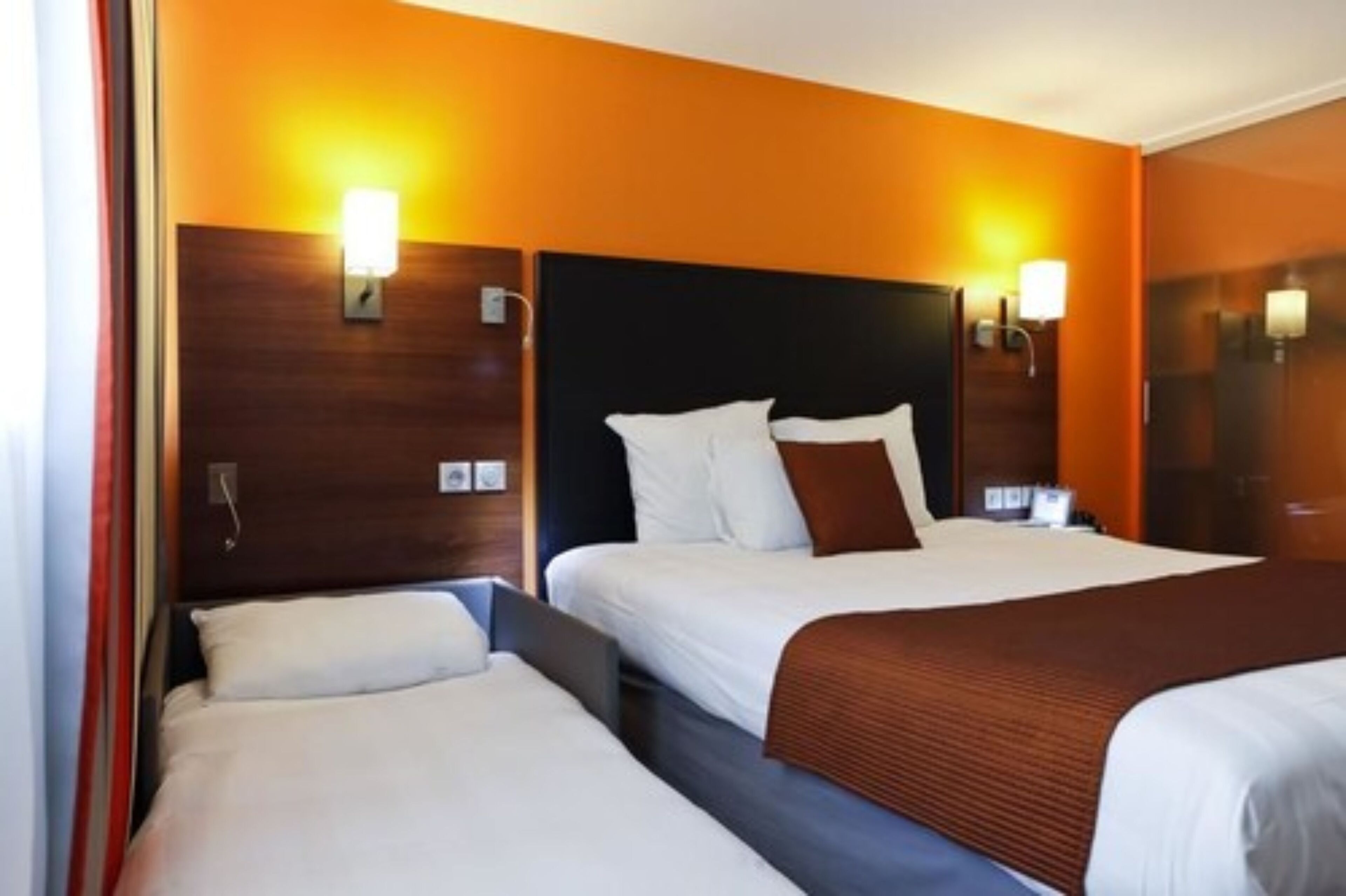 Une chambre d’hôtel avec deux lits, des têtes de lit en bois et des lampes fixées au mur.