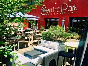 CentralPark Restaurant with outdoor seating, including wicker chairs and tables, surrounded by greenery.