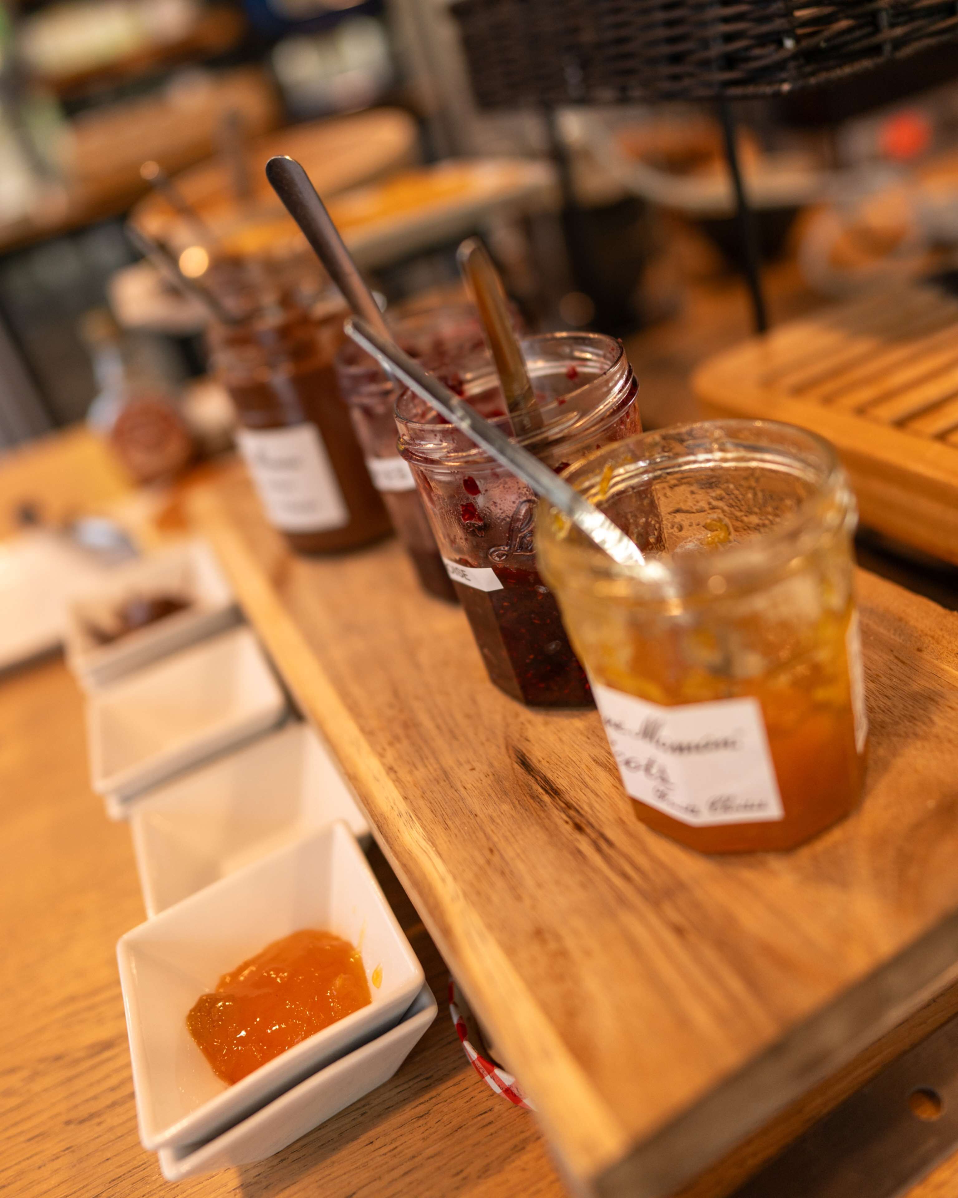 Une table en bois, avec des pots de confiture et une cuillère dans l’un des pots.