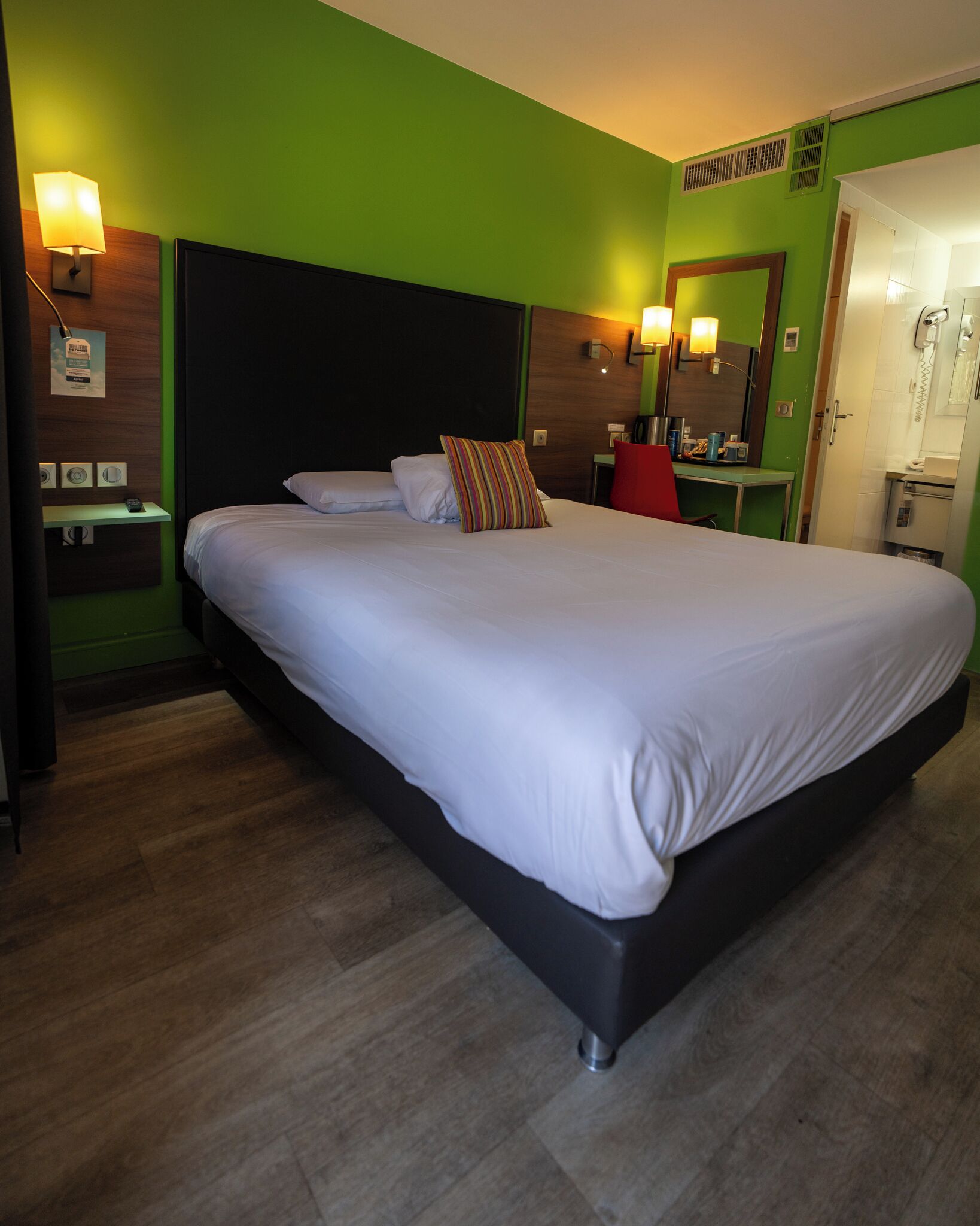 A hotel room with a large bed, a desk, a chair, a mirror, and a bathroom.