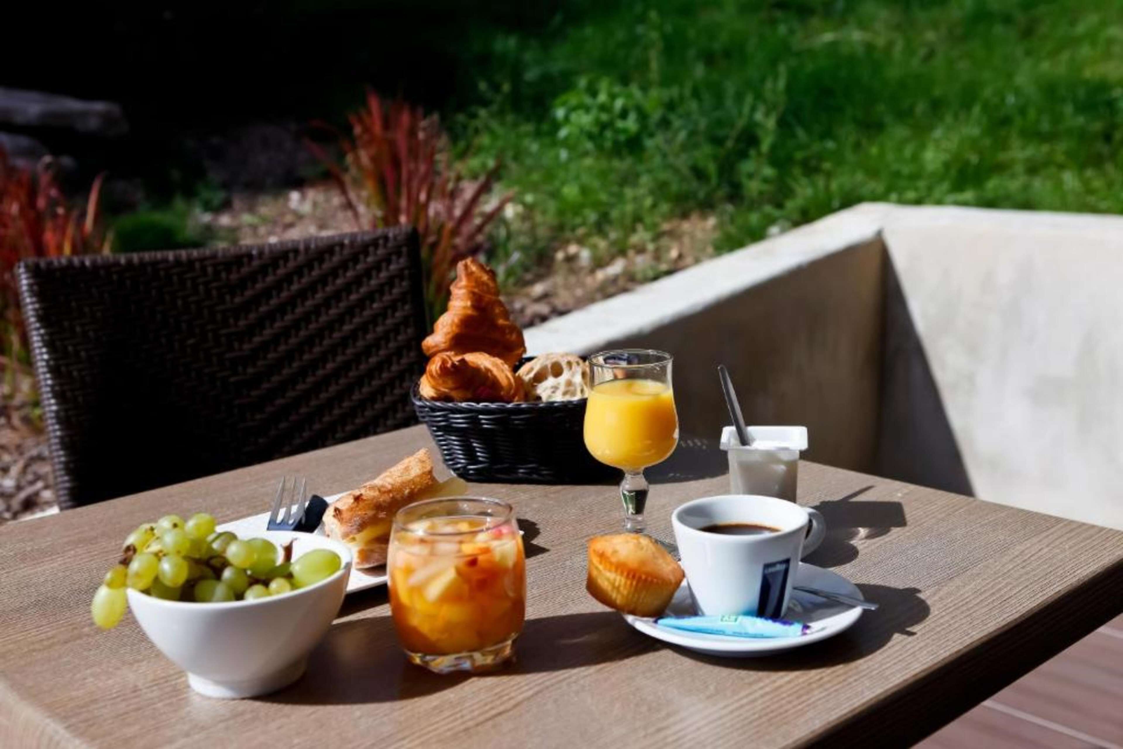 A breakfast table with a bowl of grapes, croissants, a muffin, a glass of orange juice, and a cup of coffee.