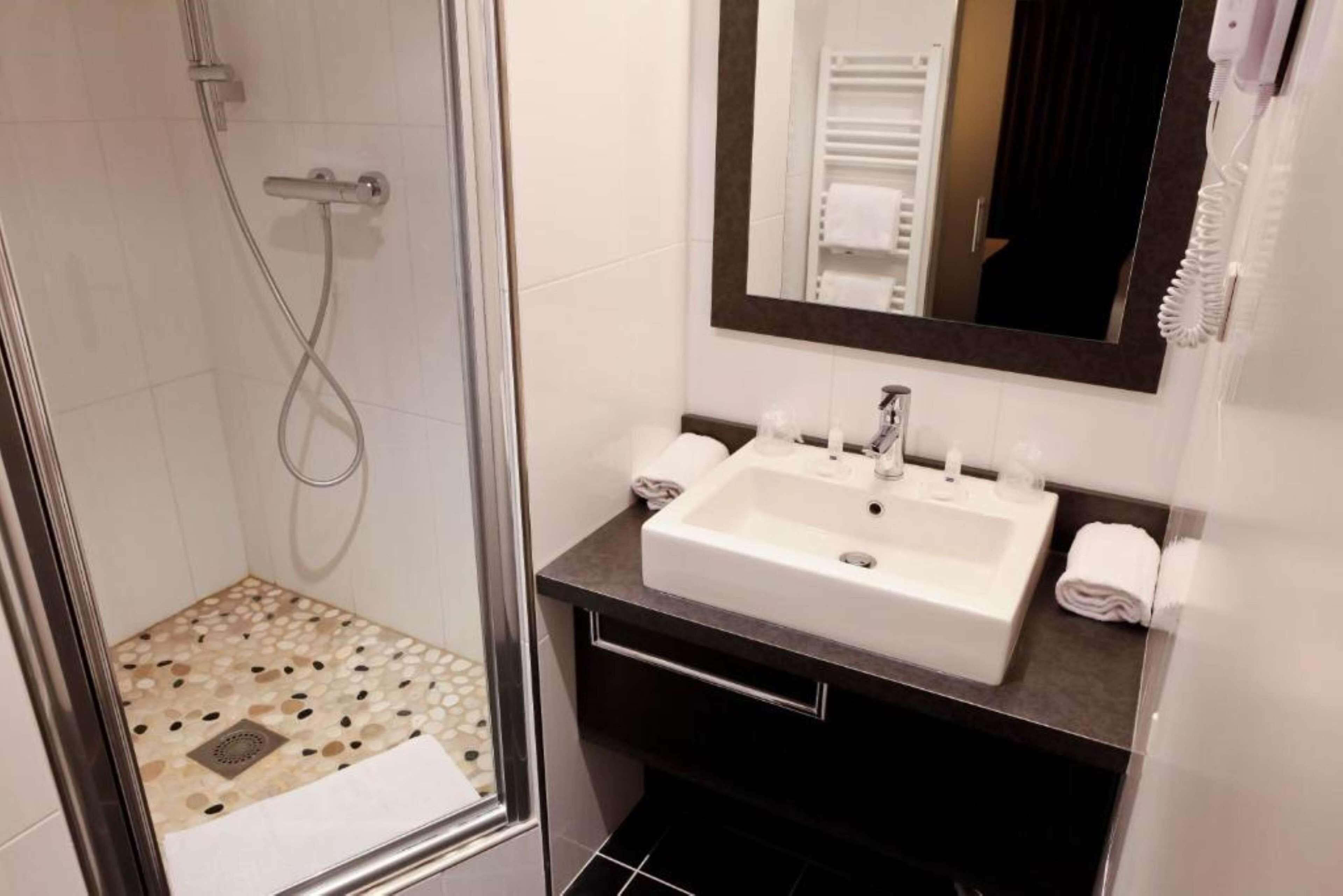 Une salle de bain moderne avec une douche à parois de verre, un lavabo blanc et un grand miroir.
