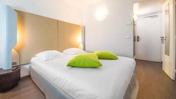 Een hotelkamer met een bed, twee kussens, een nachtkastje, een lamp en een deur.