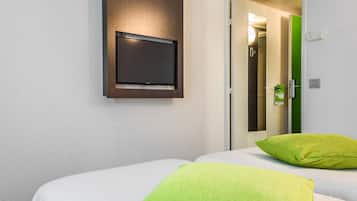 Habitación de hotel con una cama, un televisor montado en la pared y una puerta que da a un baño.