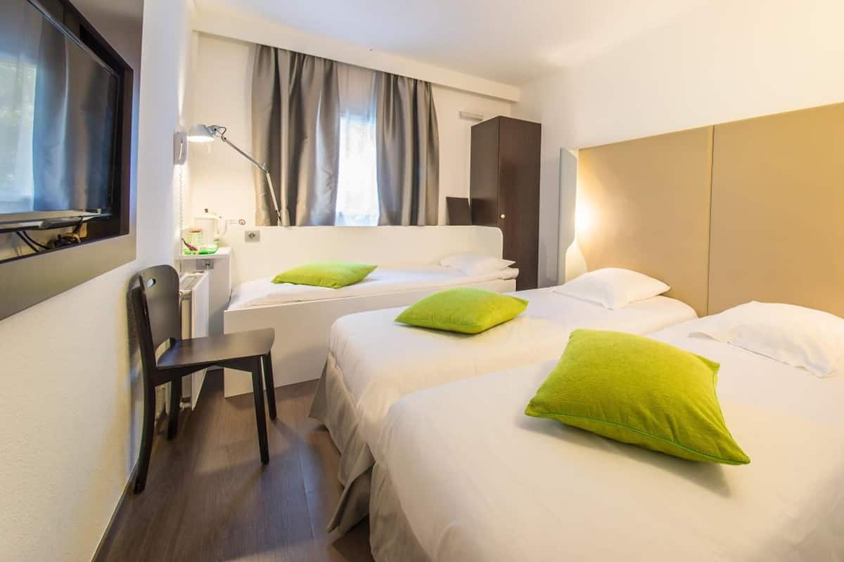 A hotel room with two beds, a desk, a chair, a TV, and a wardrobe.