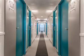 A corridor with teal doors, numbered 101 and 112, leading to a bright room at the end. - Mandarina Luxembourg Airport Hotel (Niederanven)