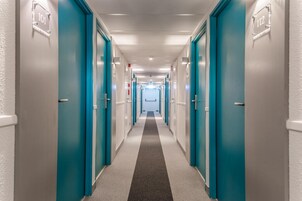 Un pasillo con puertas color turquesa, números 101 y 112, que conduce a una habitación luminosa al final.
