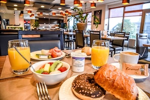 A breakfast setting with a fruit bowl, croissant, juice, coffee, and a pastry on a table.