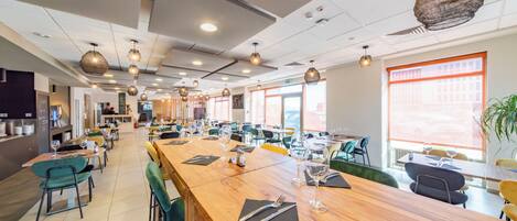 Un comedor amplio con largas mesas de madera, sillas tapizadas de verde e iluminación colgante.