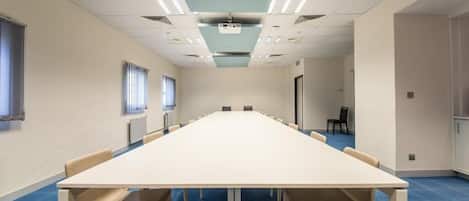 A conference room with a long table and chairs, white walls, and a blue carpet.