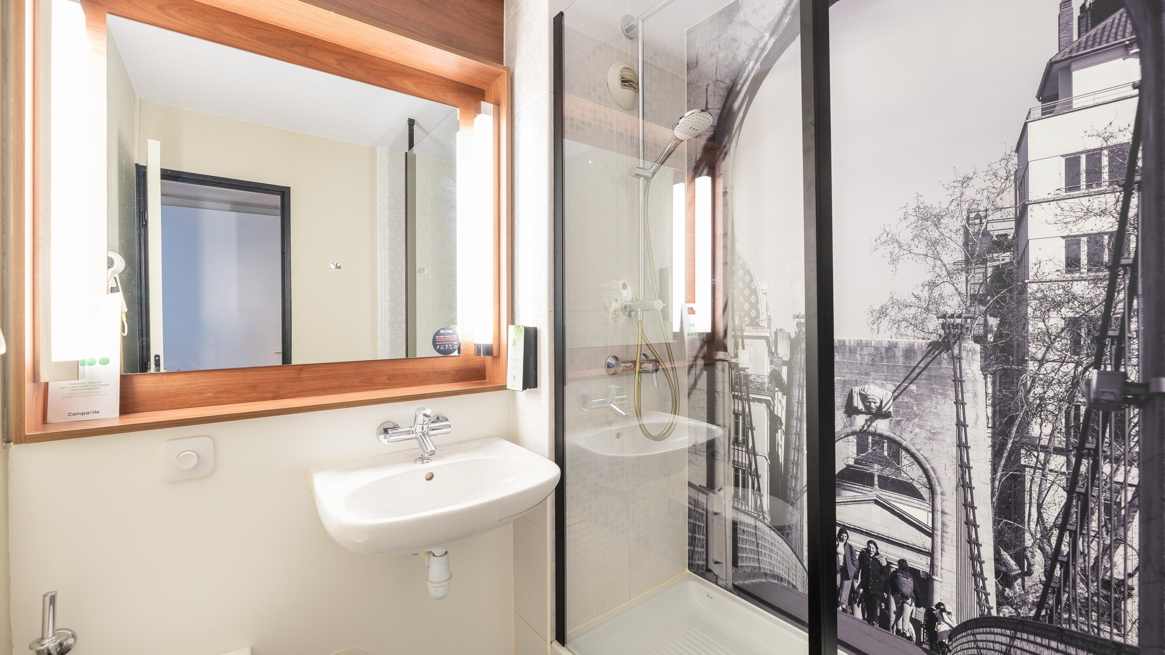Un baño con lavamanos blanco, un espejo y cabina de ducha con puerta de cristal.
