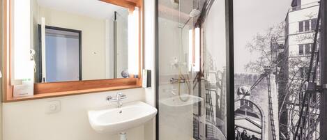 Un baño con lavamanos blanco, un espejo y cabina de ducha con puerta de cristal.