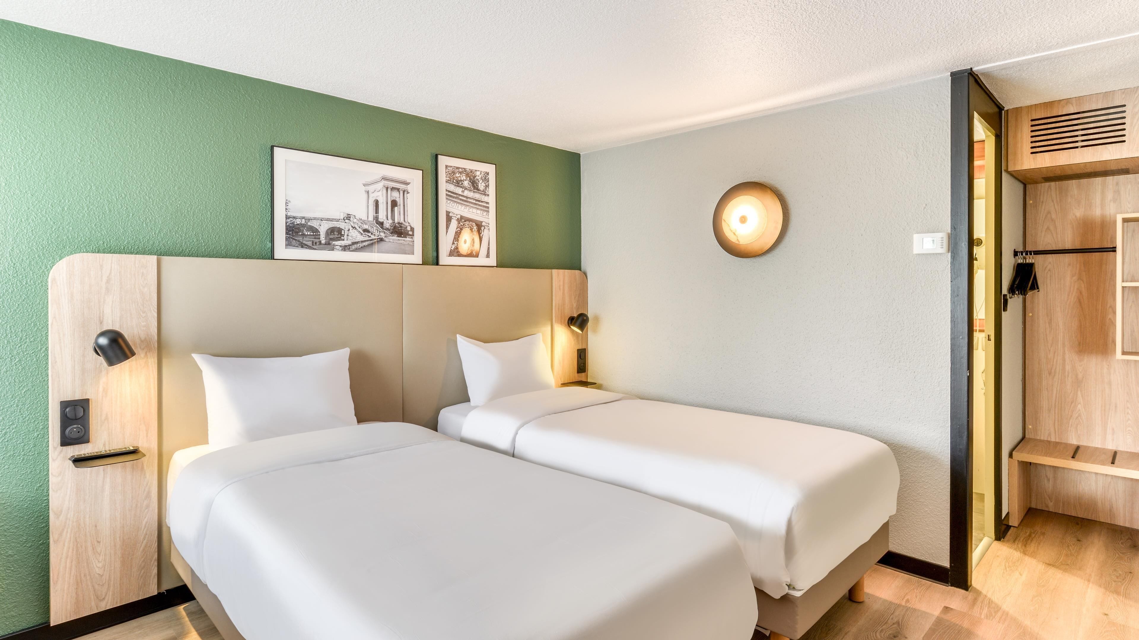 Habitació d'hotel amb dos llits, una paret verda i un quadre al damunt dels llits.