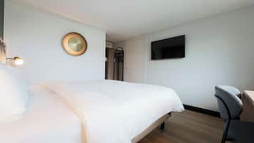 A hotel room with a large bed, a desk, a chair, a TV mounted on the wall, and a circular light fixture.