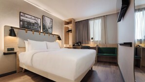 Una camera d'albergo moderna con un letto grande, una scrivania, una sedia, un armadio e una TV a parete.