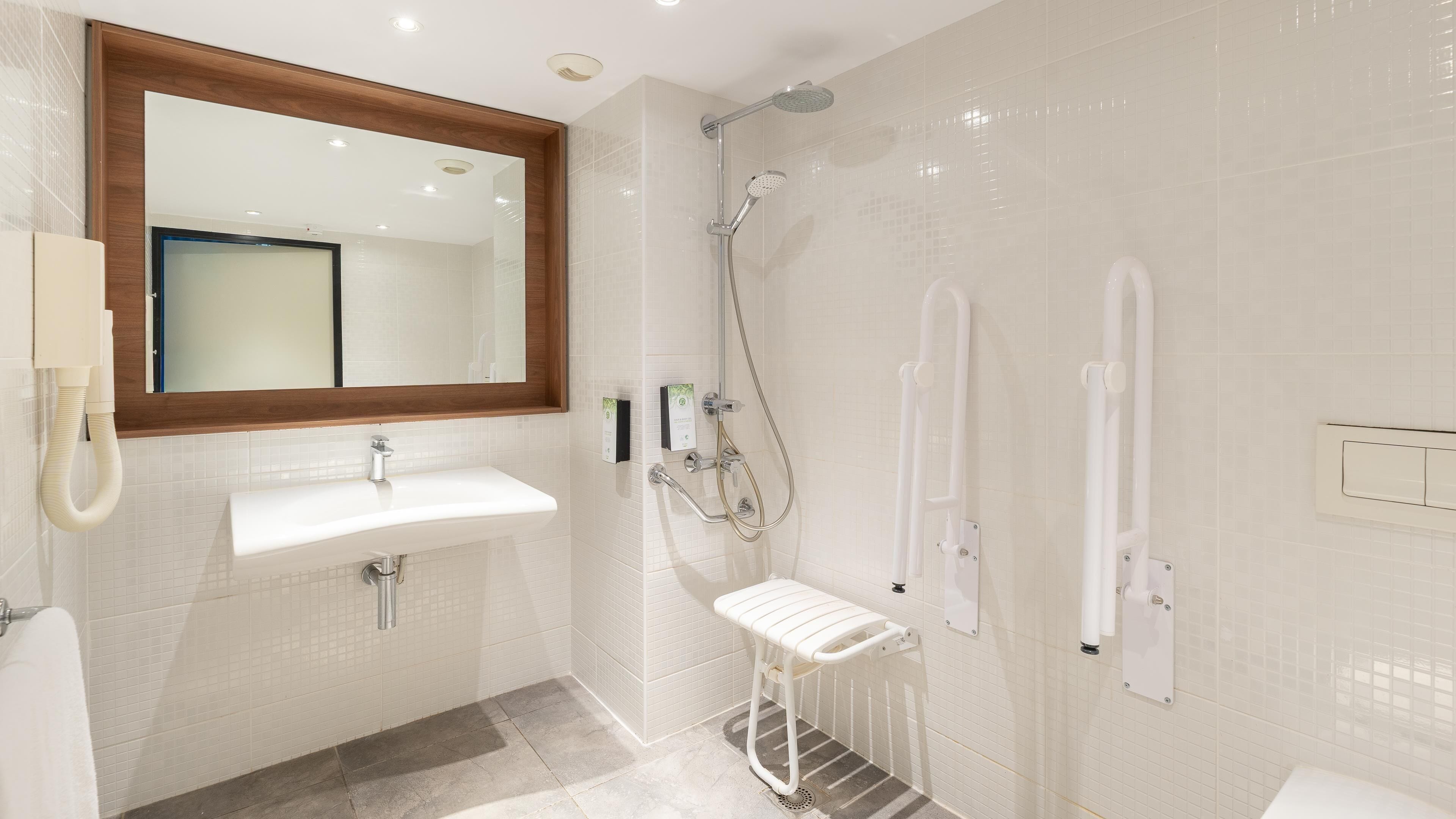 A modern bathroom with a white sink, a mirror with a wooden frame, a handheld showerhead, and a towel rack.