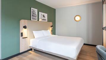 Een net opgemaakt bed in een kamer met groene wanden, met daarboven twee ingelijste foto's en een wandlamp.