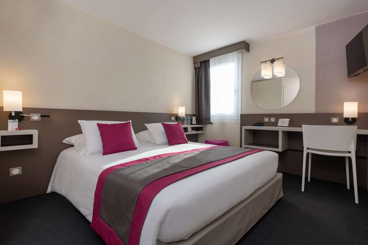 A hotel room with a large bed, bedside tables, a desk, a chair, a mirror, and a TV.