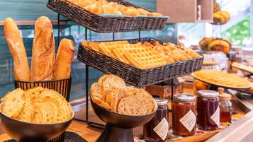Eine Verkaufstheke einer Bäckerei mit verschiedenen Brotsorten und Backwaren, darunter Baguettes, Croissants und Waffeln, sowie Gläsern mit Marmelade und Honig.