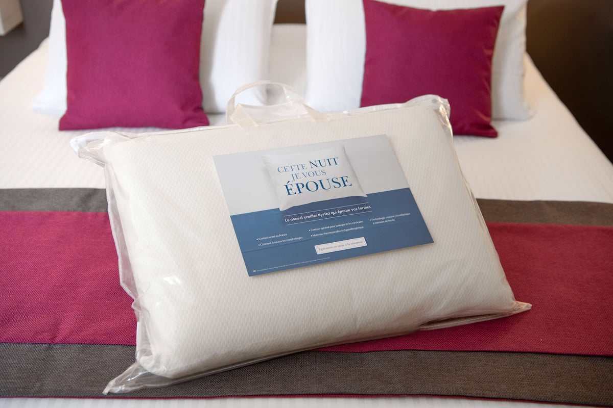 A bed with a white pillow and a tag that reads "CETTE NOUIT JE VOUS ÉPOUSE".