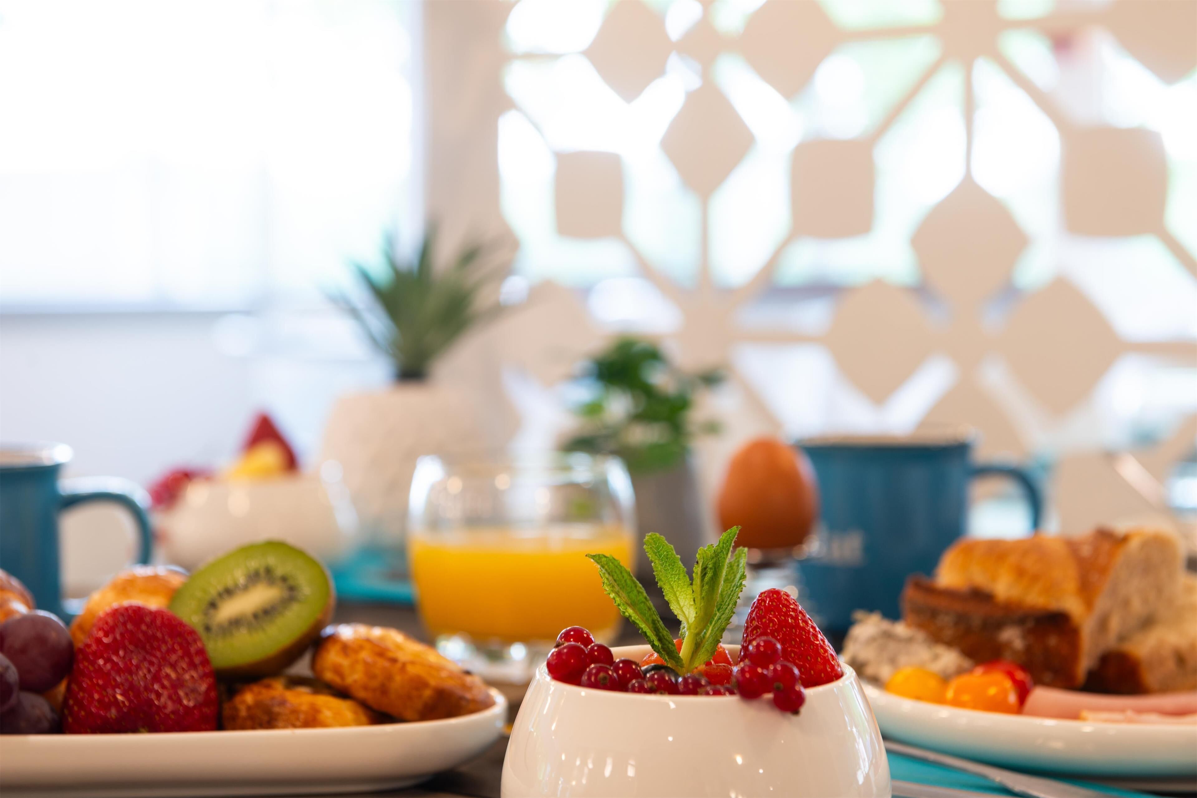 Una mesa con frutas variadas, pasteles y un vaso de jugo de naranja para el desayuno.