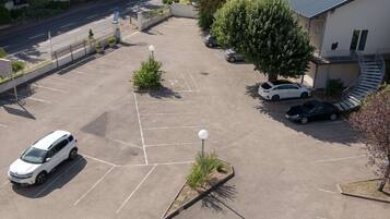 Vista aérea de un estacionamiento con varios coches, un pequeño área ajardinada con plantas y un edificio con una escalera de caracol.