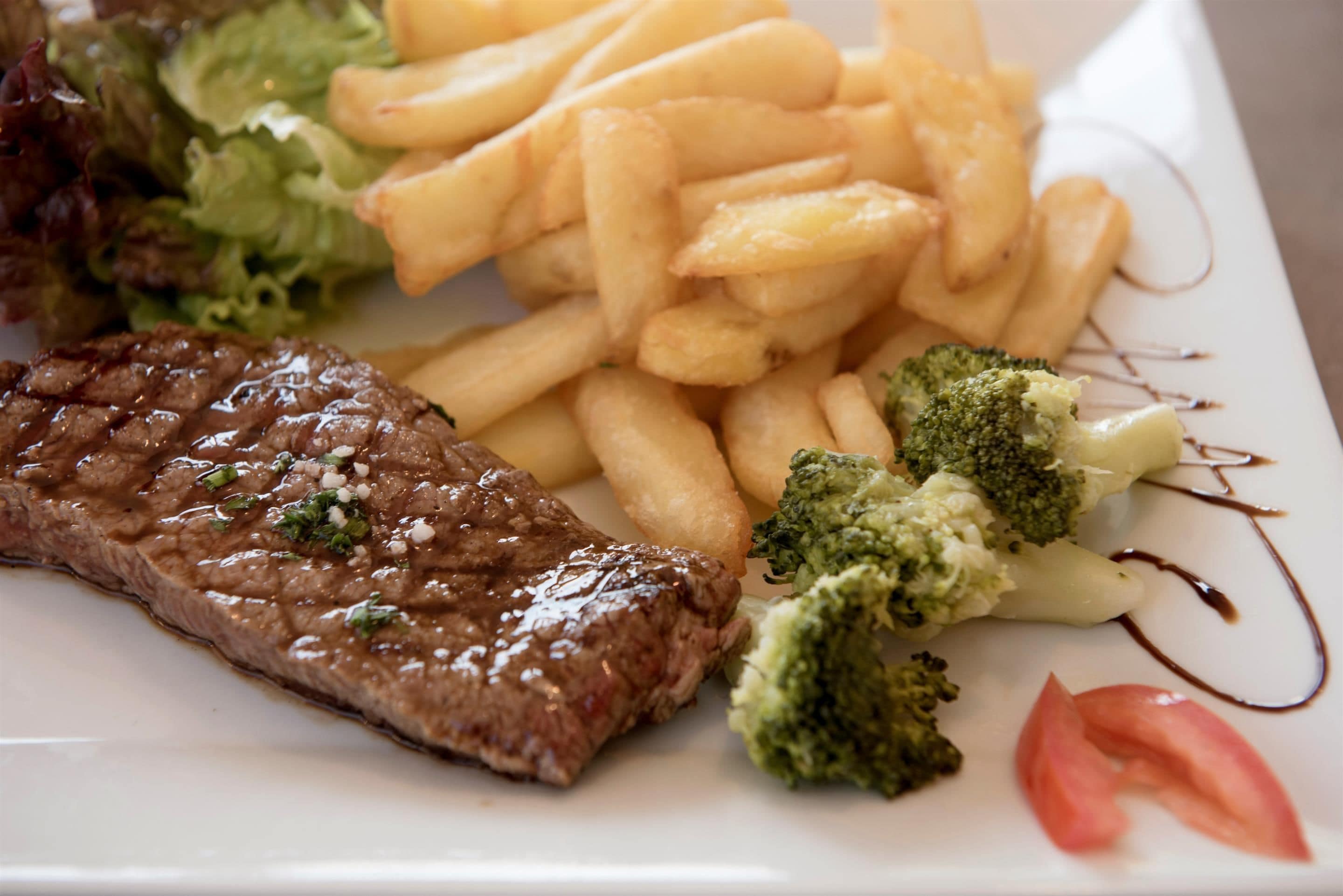 A plate with steak, fries, broccoli, and a tomato slice.