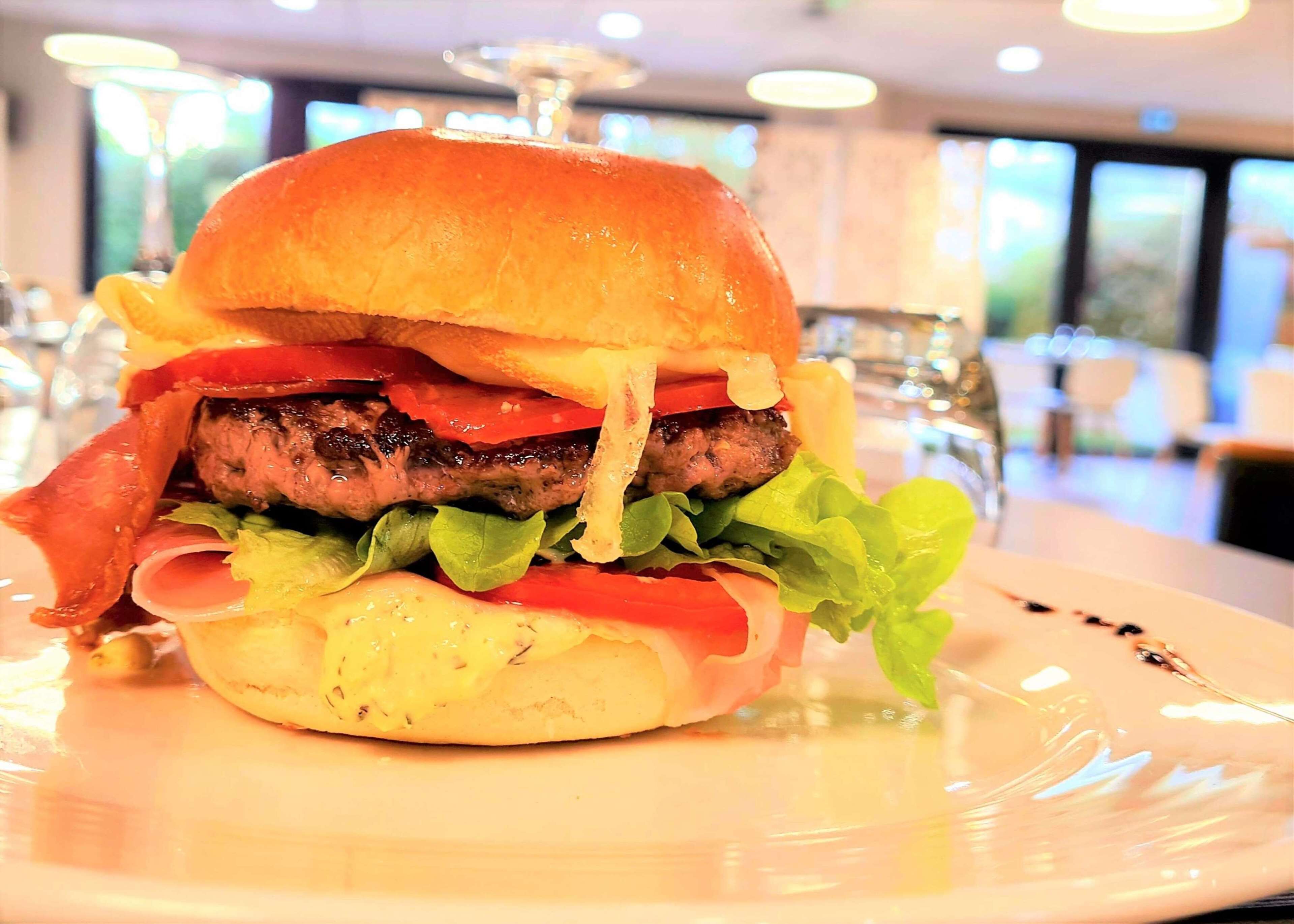 A close-up of a gourmet burger with lettuce, tomato, and bacon on a white plate.