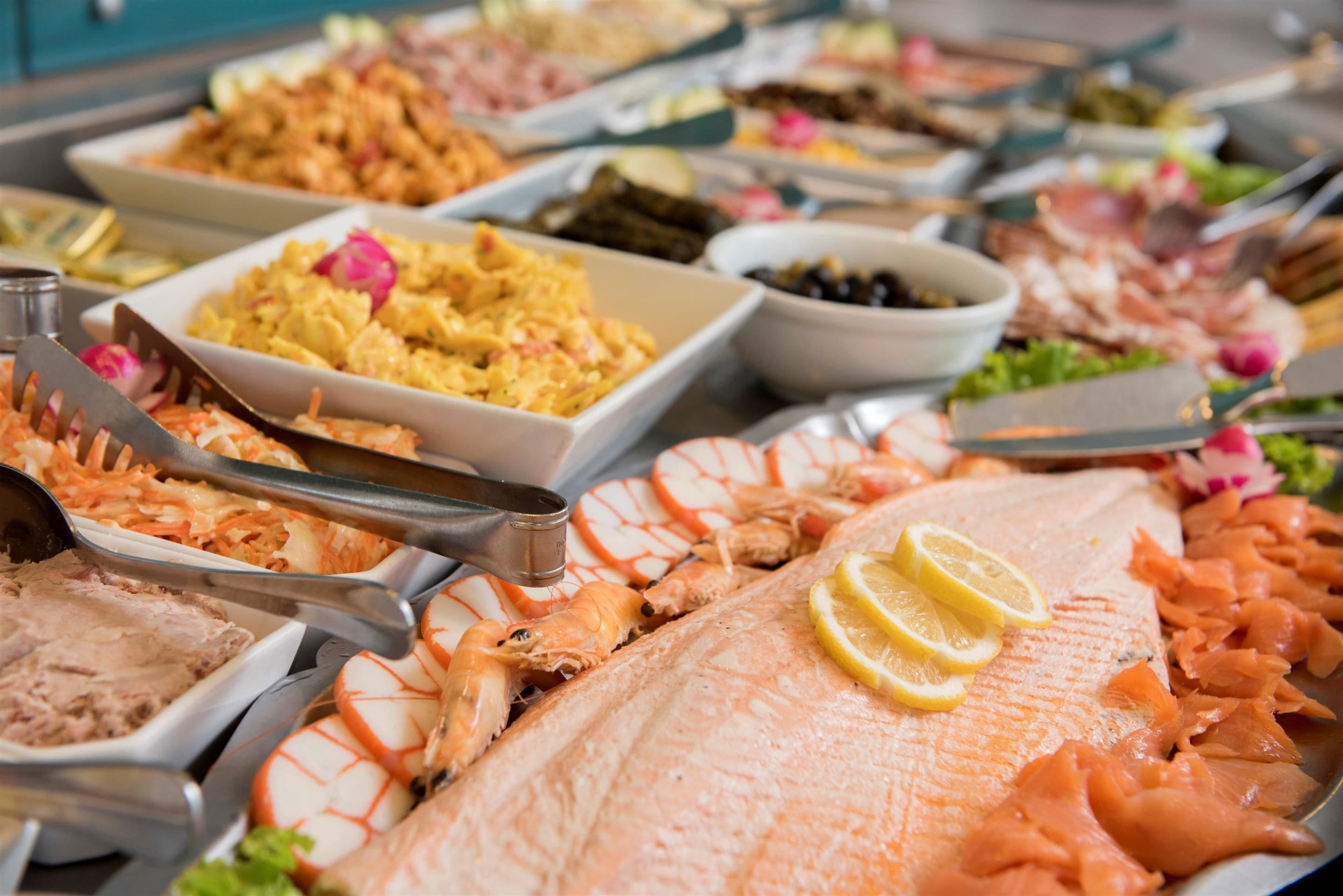 Un bufé con diversos platos, incluyendo pescado, camarones y ensaladas.