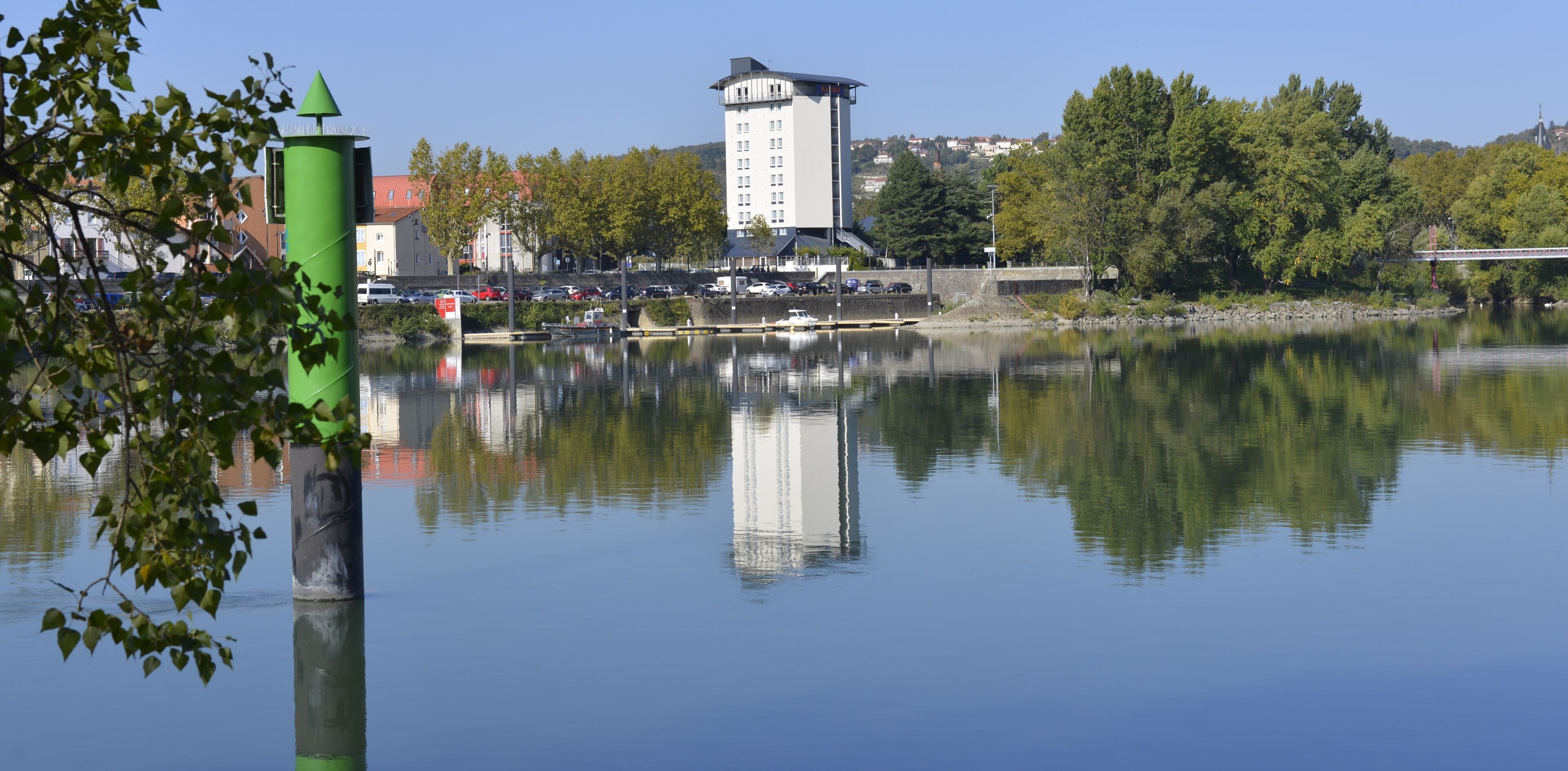 Un lac paisible, avec une bouée verte et un grand immeuble en arrière-plan.