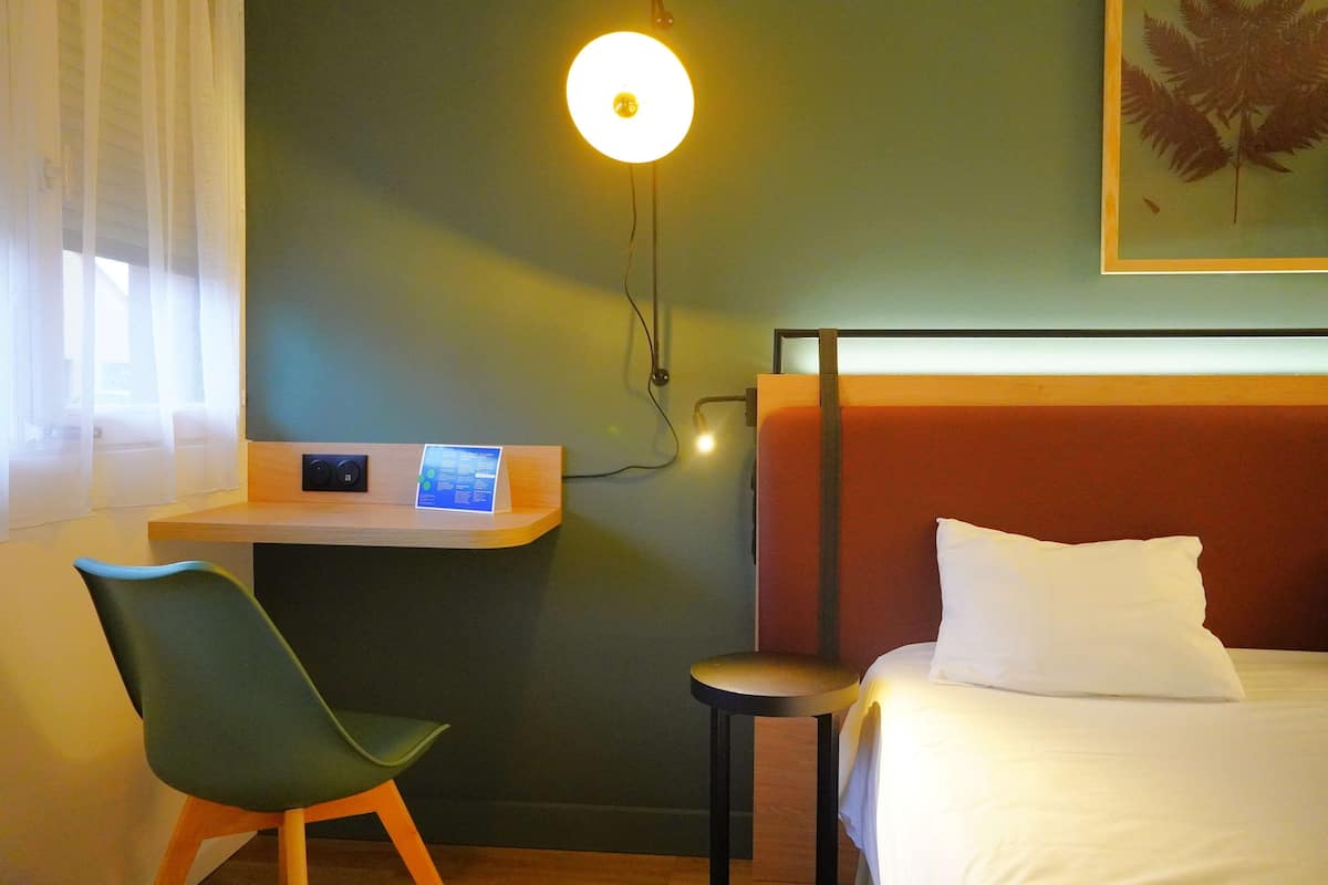 Une chambre d’hôtel équipée d’un lit, d’un bureau avec un ordinateur, d’une chaise et d’une lampe fixée au mur.