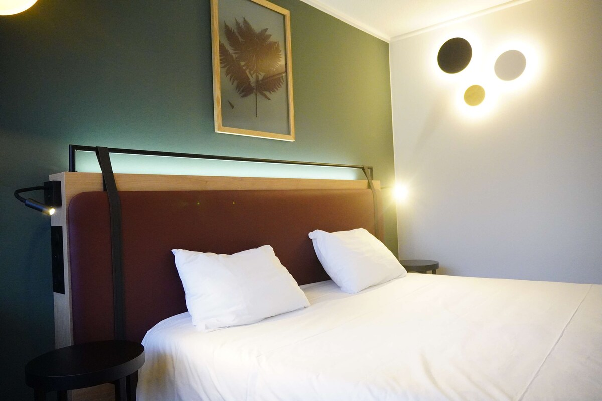 A neatly made bed with white bedding, a wooden headboard, and a framed leaf artwork on the wall.