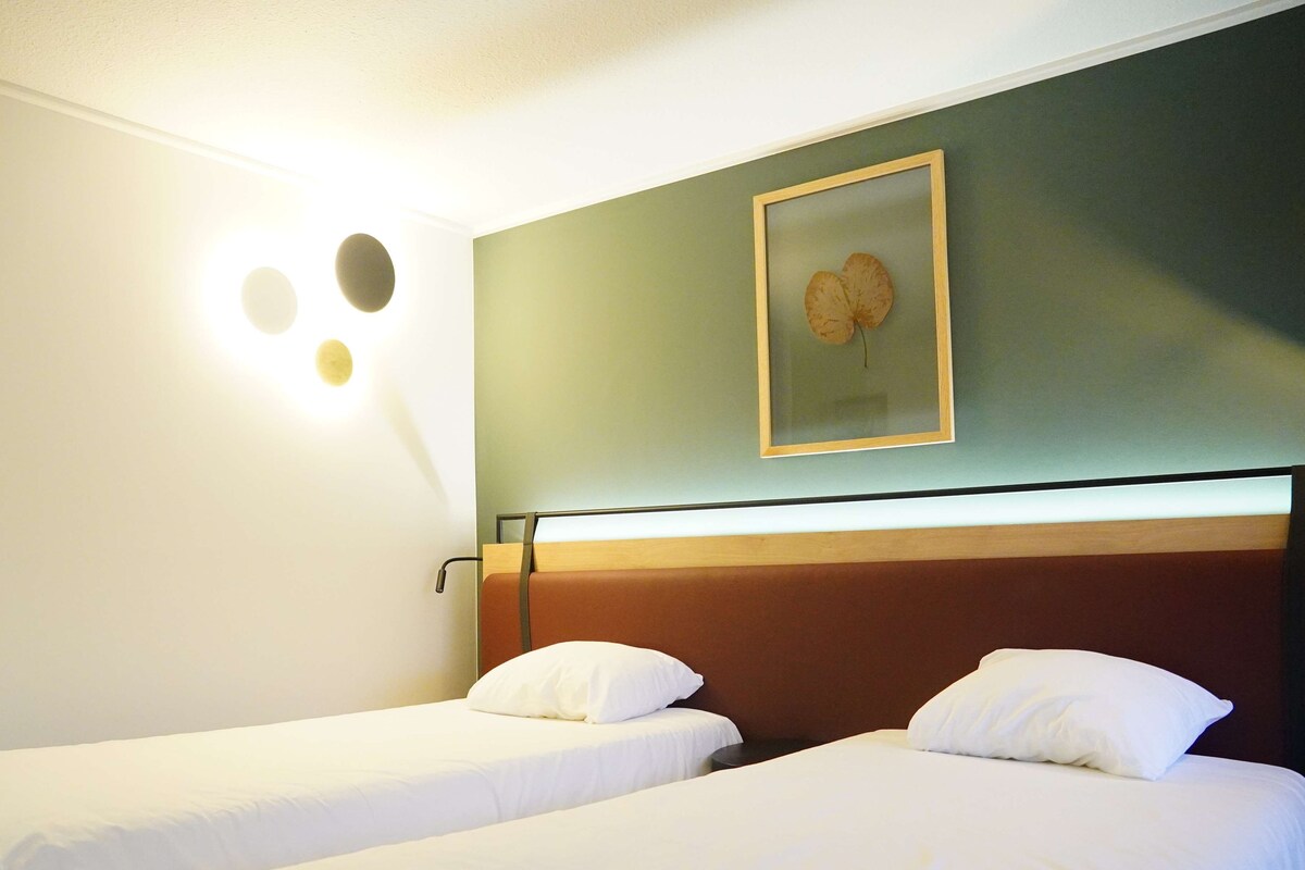A hotel room with two single beds, a wall-mounted light fixture, and a framed picture above the beds.
