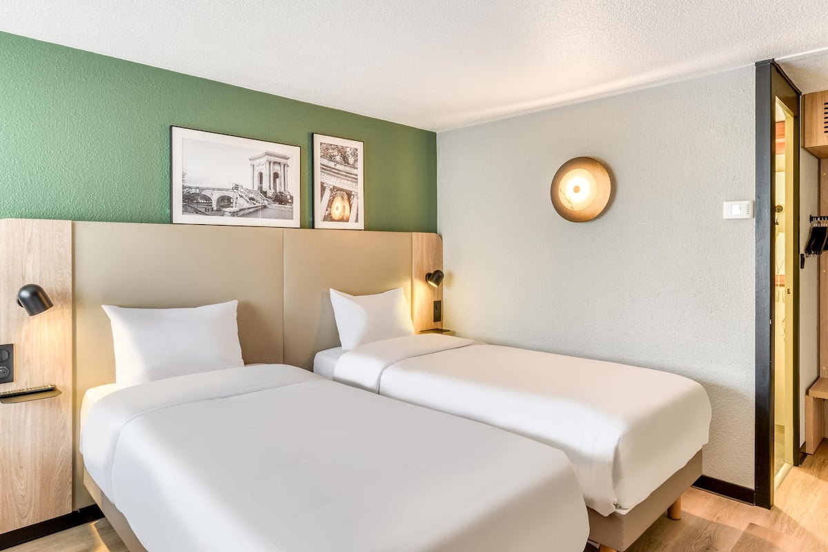 A hotel room with two beds, a green wall, and a framed picture above the beds.
