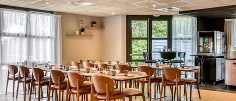 A dining area with multiple tables and chairs, a kitchen area with an oven, and large windows providing natural light.