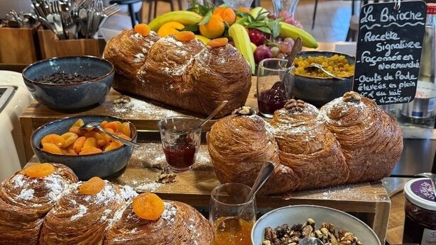Un buffet de petit-déjeuner proposant des viennoiseries, des fruits et un panneau indiquant le menu.