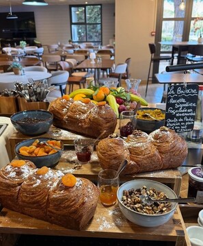 Un buffet de petit-déjeuner proposant des viennoiseries, des fruits et un panneau indiquant le menu.