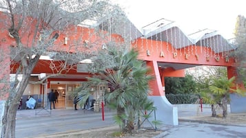 A building with a red facade and a large overhang. There are palm trees in front of the building.