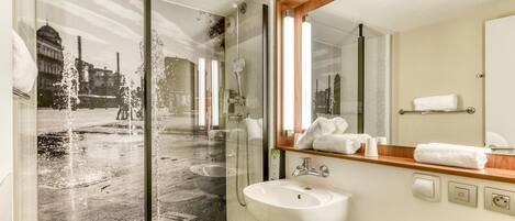 A modern bathroom with a glass shower enclosure, a white sink, and a mirror reflecting a cityscape.