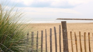 Une plage avec une clôture en bois et, au loin, un promontoire rocheux.