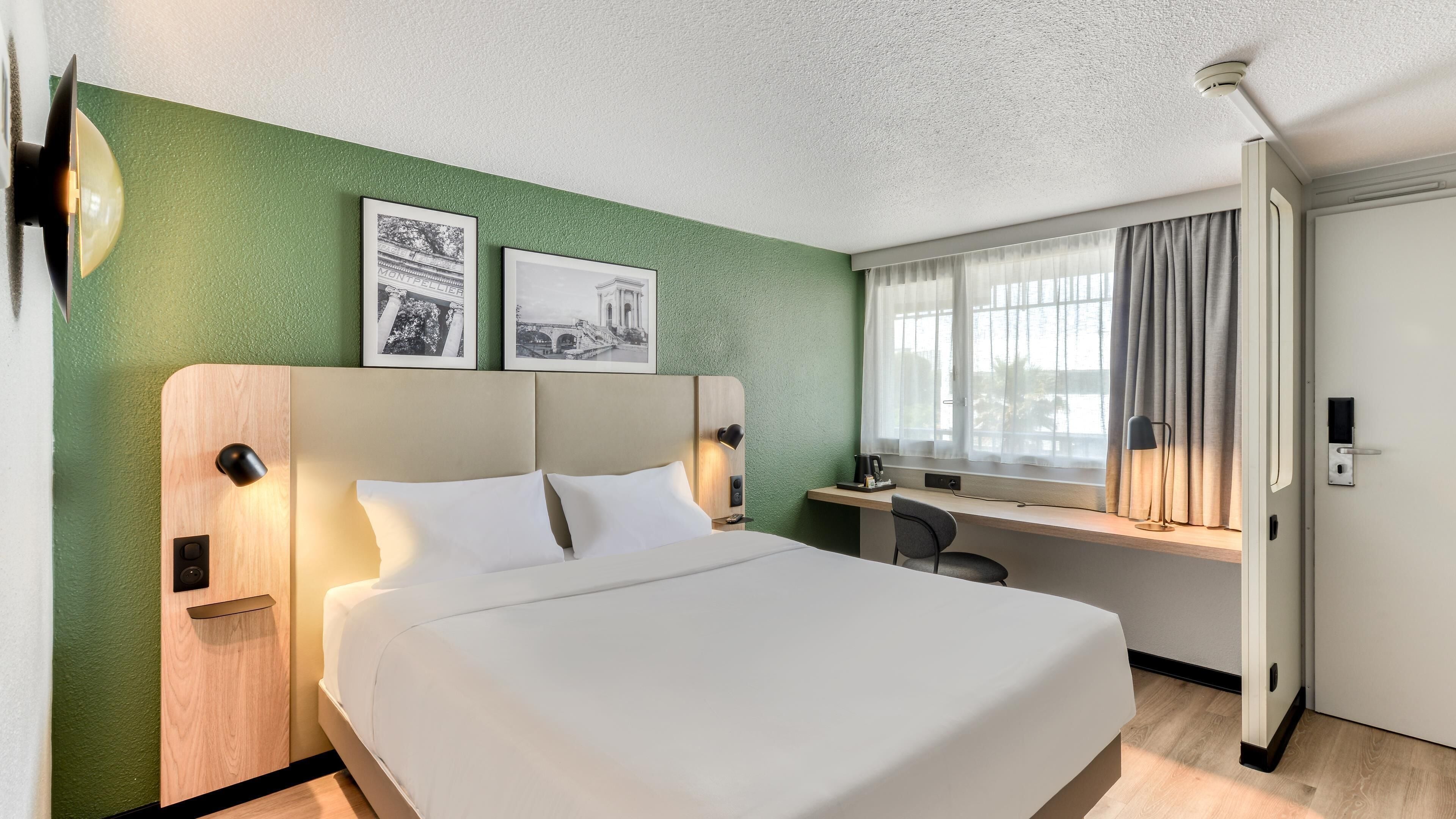 A hotel room with a bed, desk, and window.
