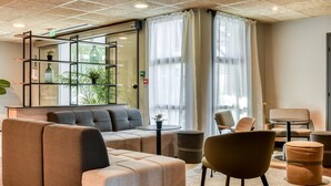 Un hall d’entrée moderne avec un canapé, des fauteuils, une petite table et une étagère décorative agrémentée de plantes.