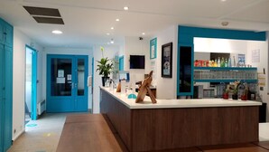 A reception area with a wooden reception desk, a potted plant, a digital screen, and a bar area with glassware and bottles.