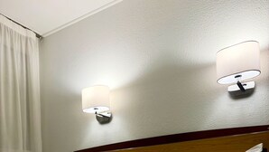 A hotel room with a neatly made bed, two wall-mounted lamps, and a wooden headboard.