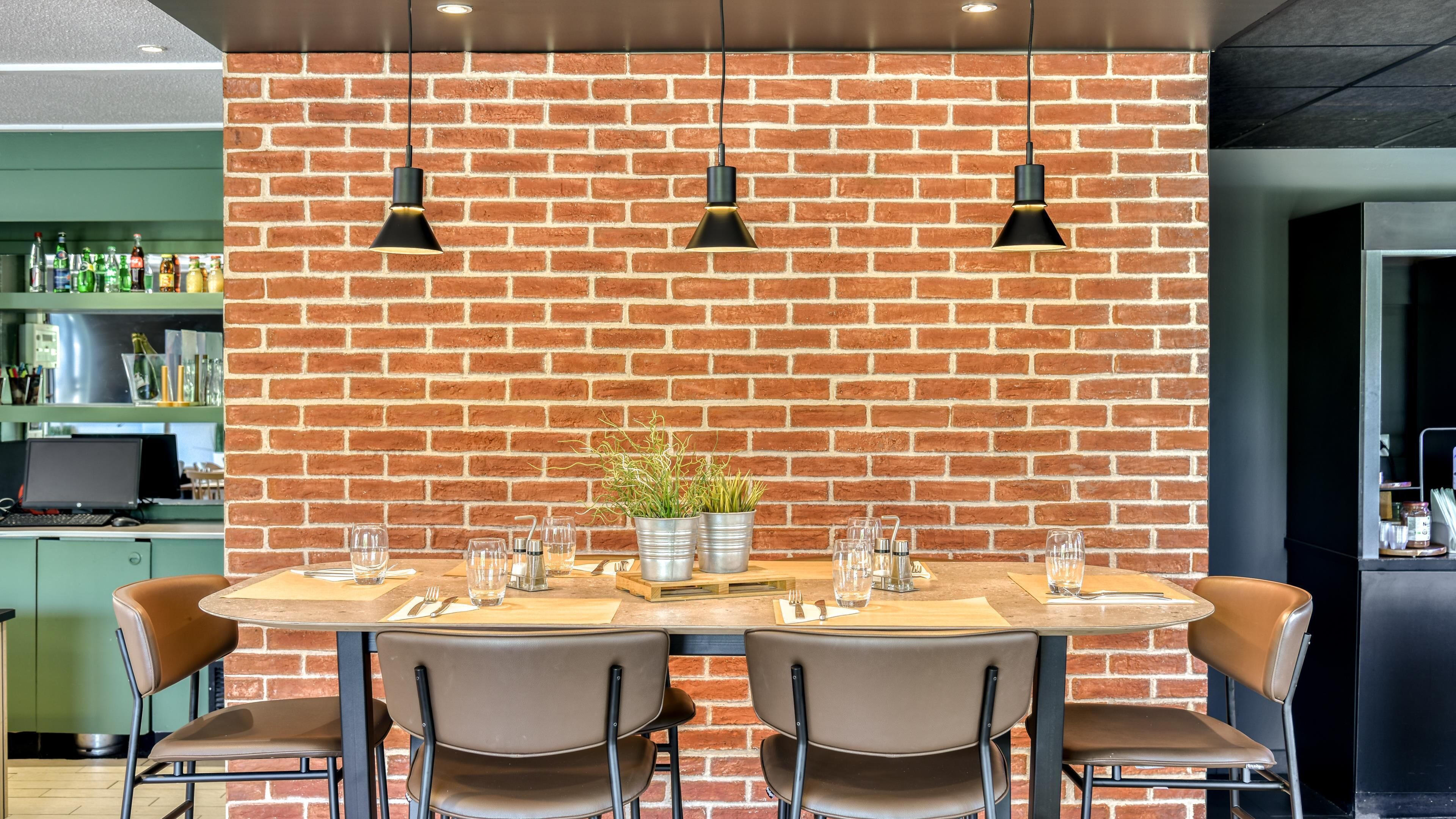 Un comedor con pared de ladrillo, una mesa redonda para cuatro personas y lámparas colgantes.