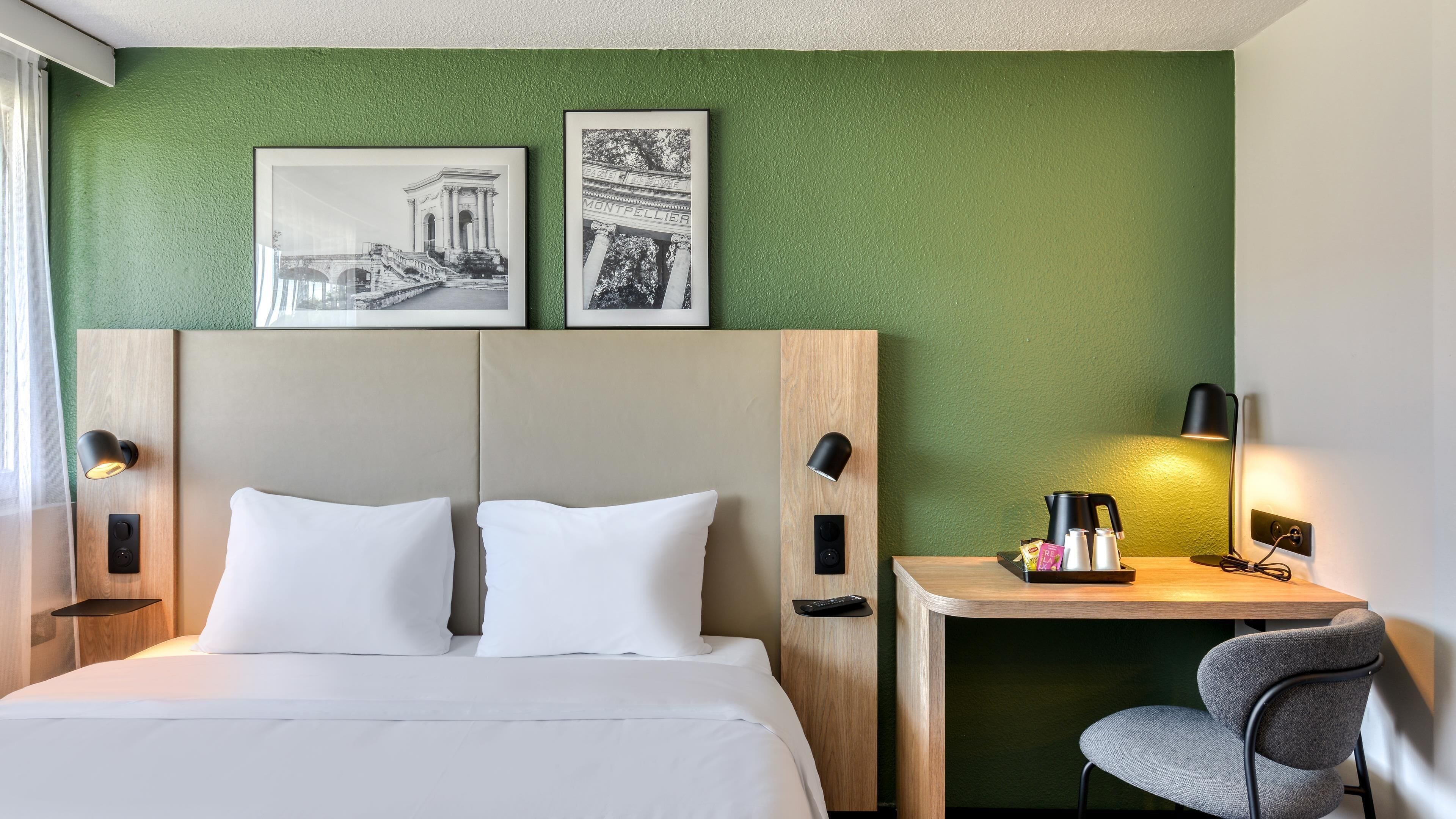 Ein Hotelzimmer mit einem Bett, einem Schreibtisch, einem Sessel und zwei gerahmten Bildern an der Wand.