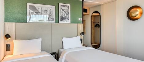 Habitación de hotel con dos camas, una pared verde con textura y un espejo con marco dorado.