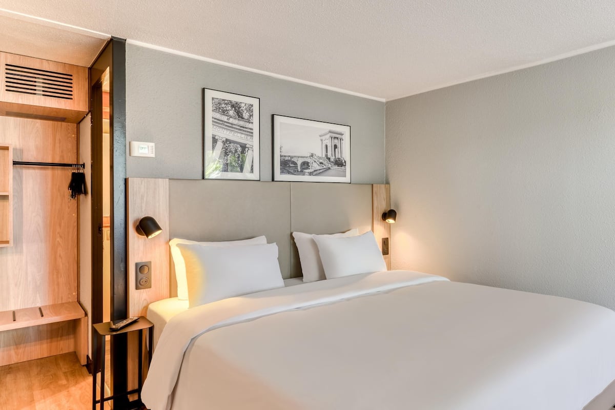 Een hotelkamer met een groot bed, twee nachtkastjes, een kledingkast en twee aan de muur hangende fotolijstjes.